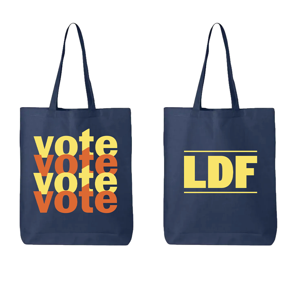 Two navy blue canvas tote bags shown side by side on a white background. The left bag features the word 'vote' printed repeatedly in a stacked, bold yellow and orange font.